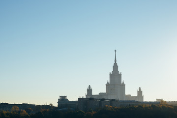 Moscow landscape. Moscow University building in morning haze behind autumn colored trees and smaller buildings. There is lot of negative space in clear sky with the sunrise glow on the right side.