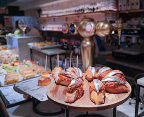 Traditional spanish snacks, appetizers or tapas called pintxos in a bar or cafe in San Sebastian, Basque country, Spain. Anchovy sandwich on a bar counter in a typical restaurant or tapas bar.