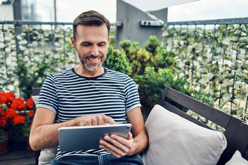 Relaxed man sitting on patio using tablet