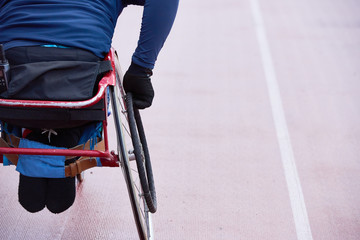Rear view of physically impaired athlete moving in racing wheelchair on track