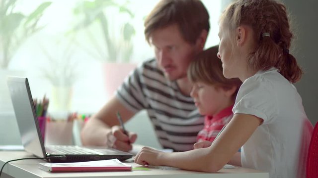 Cute children use laptop for education, online study, home studying, Boy and Girl have homework at distance learning. Lifestyle concept for Family quarantine covid-19. Father helps daughter and son.