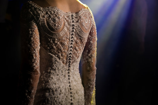 Vestido de noiva, feito de uma renda muito desenhada com bot&otilde;es alinhados para fechar nas costas. Mulher com vestido de casamento produzido por uma estilista.