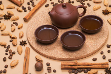 Tea set - clay tea pot with tea cups on cork stand. Coffee beans, cinnamon, almond and macadamia on background.