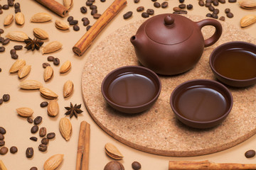 Close up tea set - clay tea pot with tea cups. Coffee beans, cinnamon, almond and macadamia on background.