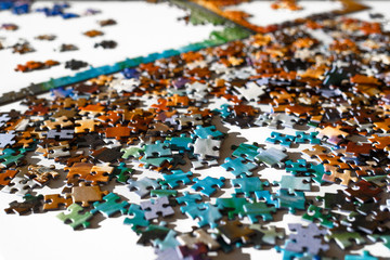 Scattered multicolored jigsaw puzzle pieces. Lying on white table in sun light. Concept of putting together elements and solving problems.