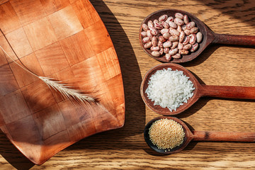 White rice, pinto beans and proso millet seeds on wooden kitchen spoons.