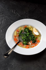 Edible wild herbs cooking. Vegetable soup with stinging nettle and boiled egg in white plate on black background