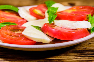 Plate with caprese salad (italian salad with cherry tomatoes, mozzarella cheese and basil leaves) on wooden table