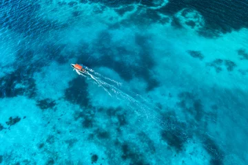 Fotobehang Aerial view of the fishing boat in clear blue water at sunset in summer. Top view from drone of yacht, sandy beach in Indian ocean. Travel in Zanzibar, Africa. Tropical landscape with motorboat, sea © den-belitsky