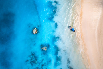 Aerial view of the fishing boat in clear blue water at sunset in summer. Top view from drone of boat, yacht, sandy beach in Zanzibar. Travel. Tropical seascape with sailboat, sea. View from above