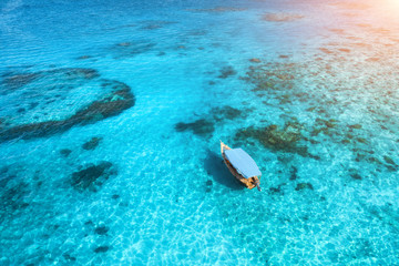 Fototapeta premium Aerial view of the fishing boat in clear blue water at sunset in summer. Top view from drone of yacht, sandy beach in Indian ocean. Travel in Zanzibar, Africa. Tropical landscape with motorboat, sea