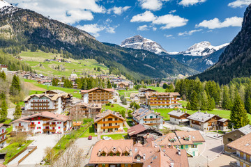 Fototapeta premium Aerial view of valley with Chalet, green slopes of the mountains of Italy, Trentino, Fontanazzo, huge clouds over a valley, roofs of houses of settlements, green meadows, Dolomites on background,