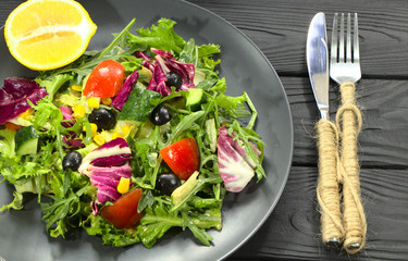 Vegetable salad on a black plate, cutlery. Gourmet food made from arugula and vegetables.