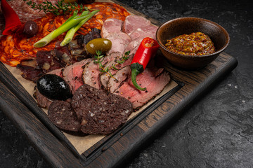 Salami sausages sliced with pepper, garlic and rosemary on cutting board on wooden table
