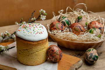 Easter cake, and Easter eggs in a wicker basket with a flowering branch on a wooden background