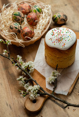 Easter cake, and Easter eggs in a wicker basket with a flowering branch on a wooden background