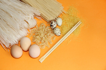 rice noodles all kinds of macaroni and macaroni with chicken, quail eggs and chopsticks on an orange background