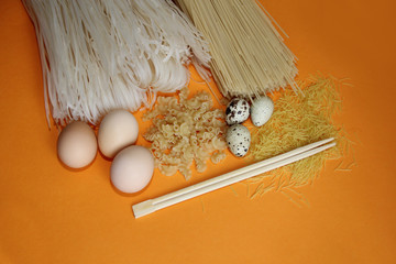 rice noodles all kinds of macaroni and macaroni with chicken, quail eggs and chopsticks on an orange background