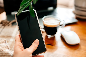Smartphone in hand .Close up.A Cup of coffee and a computer mouse in the background.Home office.Work at home.