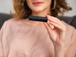 Woman's beauty blogger hand holding professional hi-end cosmetic red lipstick with blurred body...