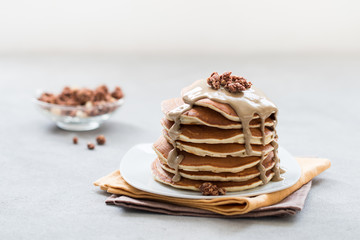 Pancake with nut paste, granola, nuts on a plate on a light gray background