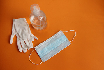 virus disinfection measures white protective gloves, sanitizer, protective mask isolated on an orange background