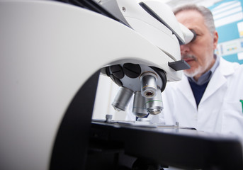 Man using microscope in laboratory, coronavirus medical research concept