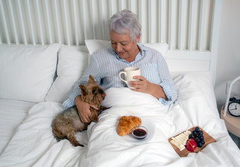 Elderly  woman having breakfast in bed with her Yorkshire Terrier