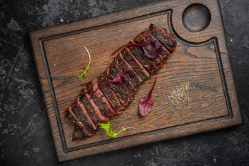 Sliced grilled beef barbecue Striploin steak with chimichurri sauce on cutting board on dark wooden background