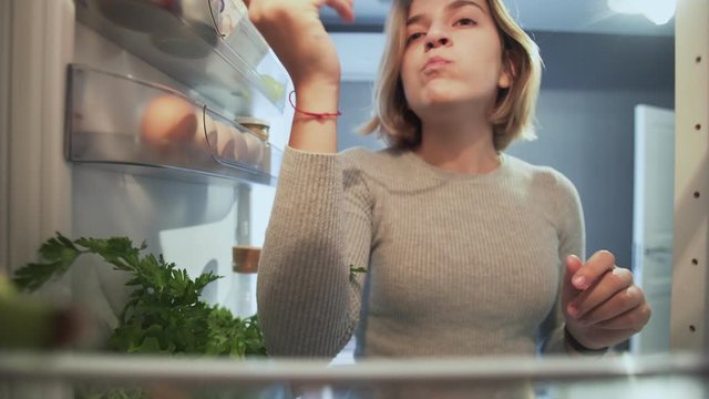 View Looking Out From Inside Of Refrigerator As Woman with fork opens door eats salad and something else