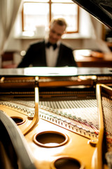 close-up photo of classical instrument piano, young guy in suit playing on it, performing classical music