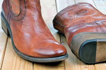 Pair of new classic leather brown cowboy boots on wooden boards. Macro shooting