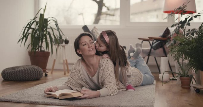 Mother reading a book while her daughter plays with her hair and kiss her stay at home virus pandemic outbreak