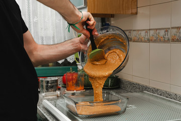 Young male cooker spilling carrot cake dough on a oven pan
