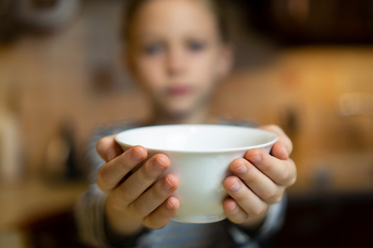 Child reaching out hands holding white empty bowl plate offering food or asking for food