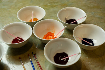White bowls plates with ear sticks and colorful powder  and paint brushes laying at the table. Easter eggs painting preparation