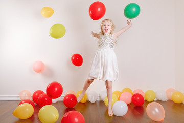 Fototapeta na wymiar Cute adorable little girl celebrating birthday at home. Lovely girl child with the colorful balloons having fun. Quarantine birthday party at home alone during COVID-19 pandemic self isolation.