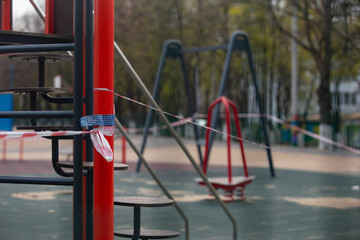 Kharkov, Ukraine, 18.04.2020:
Closed on 
quarantine by covid-19 kids playground with tied of white and red boundary tape in carantin time with warning 
sign, medium shot 