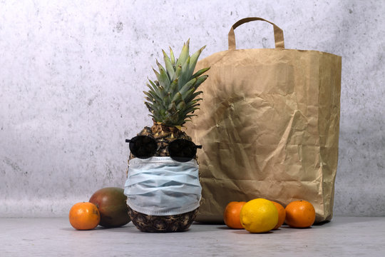 Pineapple In A Medical Mask And Sun Glasses With Other Fruits Near To The Food Box. Contactless Delivery.