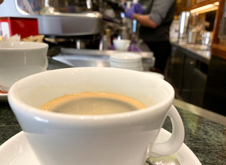 Taza de cafe, con un barista al fondo preparando bebidas