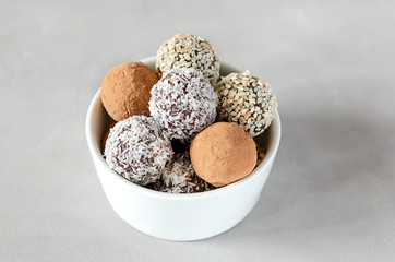 Raw vegan energy balls in a bowl. Natural sweets made from nuts and dried fruits in coconut and cocoa, close-up. The concept of paleo diet, sweets without sugar and gluten, raw food dessert.