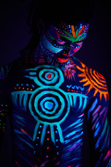 portrait of strong muscular male covered with fluorescent luminescence body art glowing on neon light