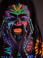 fantastic mysterious african male with UV body art posing at camera, futuristic body art, fluorescent paints glows in neon light