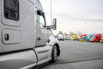 Gray bonnet big rig semi truck standing on the truck stop parking lot opposite other parked truck standing