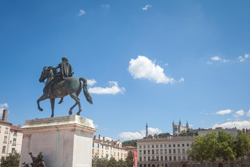 Naklejka premium Roi Louis XIV statue on the Place Bellecour Square, in downtown Lyon, with the Basilique Notre Dame de Fourviere Church in background in summer