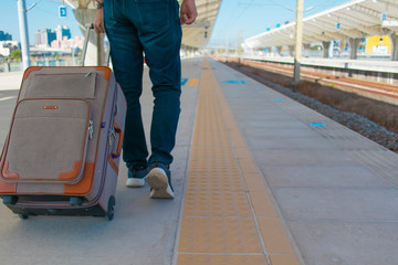 鉄道のプラットフォームをスーツケースをひきながら歩くジーンズ姿の男性
