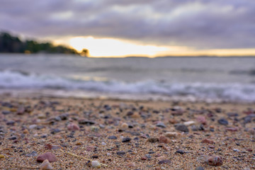 Blurred sandy beach with stones and waves on a background on a sunset.