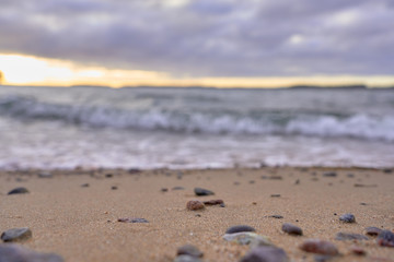 Fototapeta na wymiar Blurred sandy beach with stones and waves on a background on a sunset.
