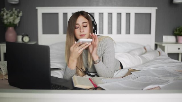 Young woman with headphones lying on the bed and taking a photo of her book