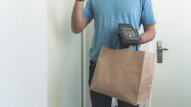 Delivery guy with protective mask holding box / bag with groceries and POS for contactless payment.